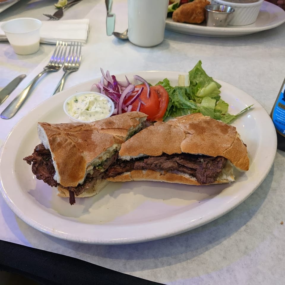 Argentinean steak sandwich with a side salad, red onions, tomato, and a small cup of sauce.