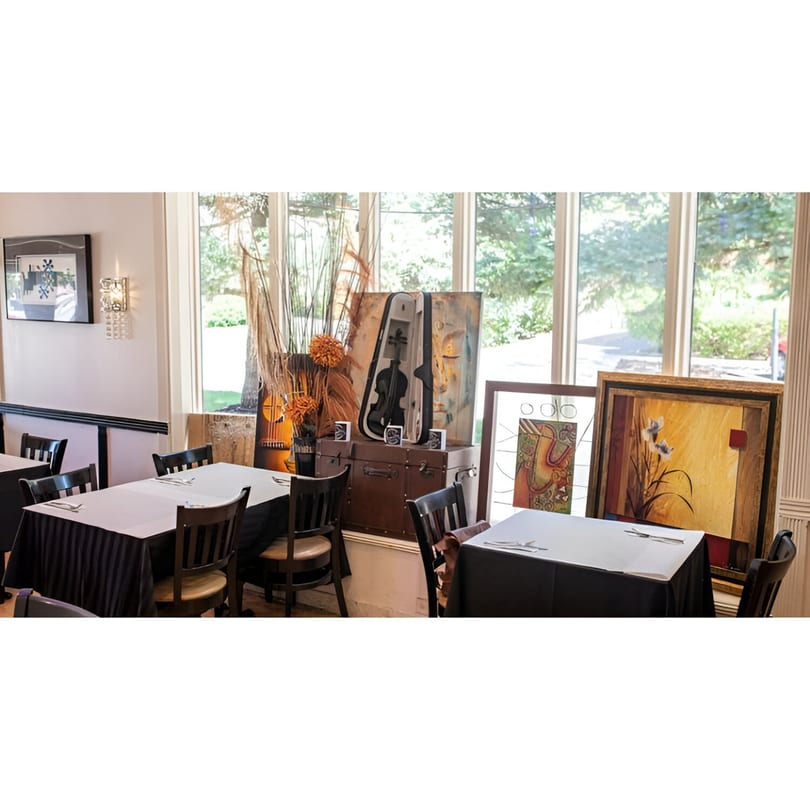 Dining room with set tables, large windows, and decorative art including a violin and guitar.