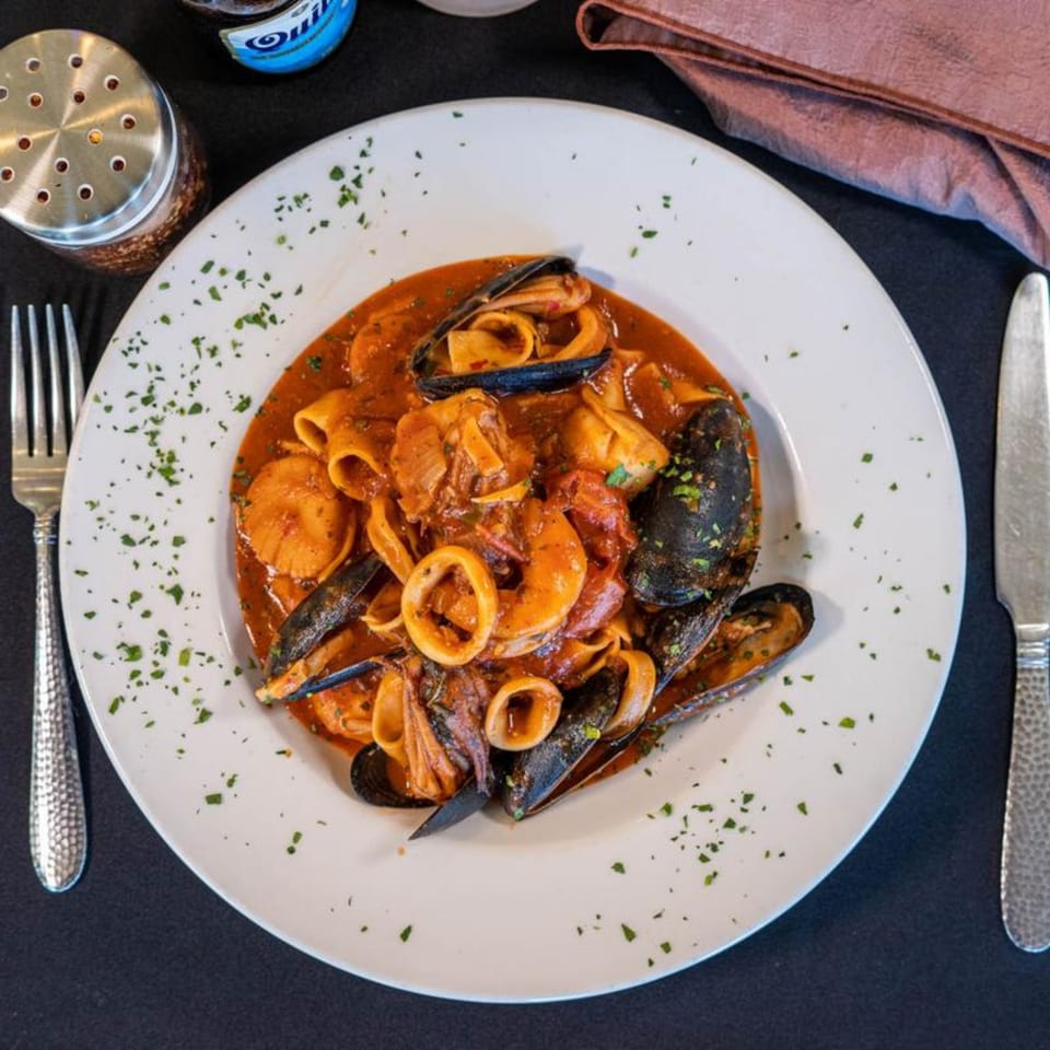 Seafood pasta with mussels, calamari, and scallops in a rich red sauce, garnished with parsley.
