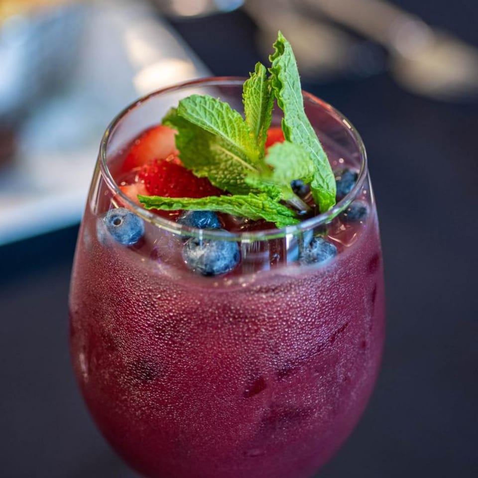 Close-up of a vibrant berry cocktail with mint, blueberries, and strawberries in a condensation-covered glass.