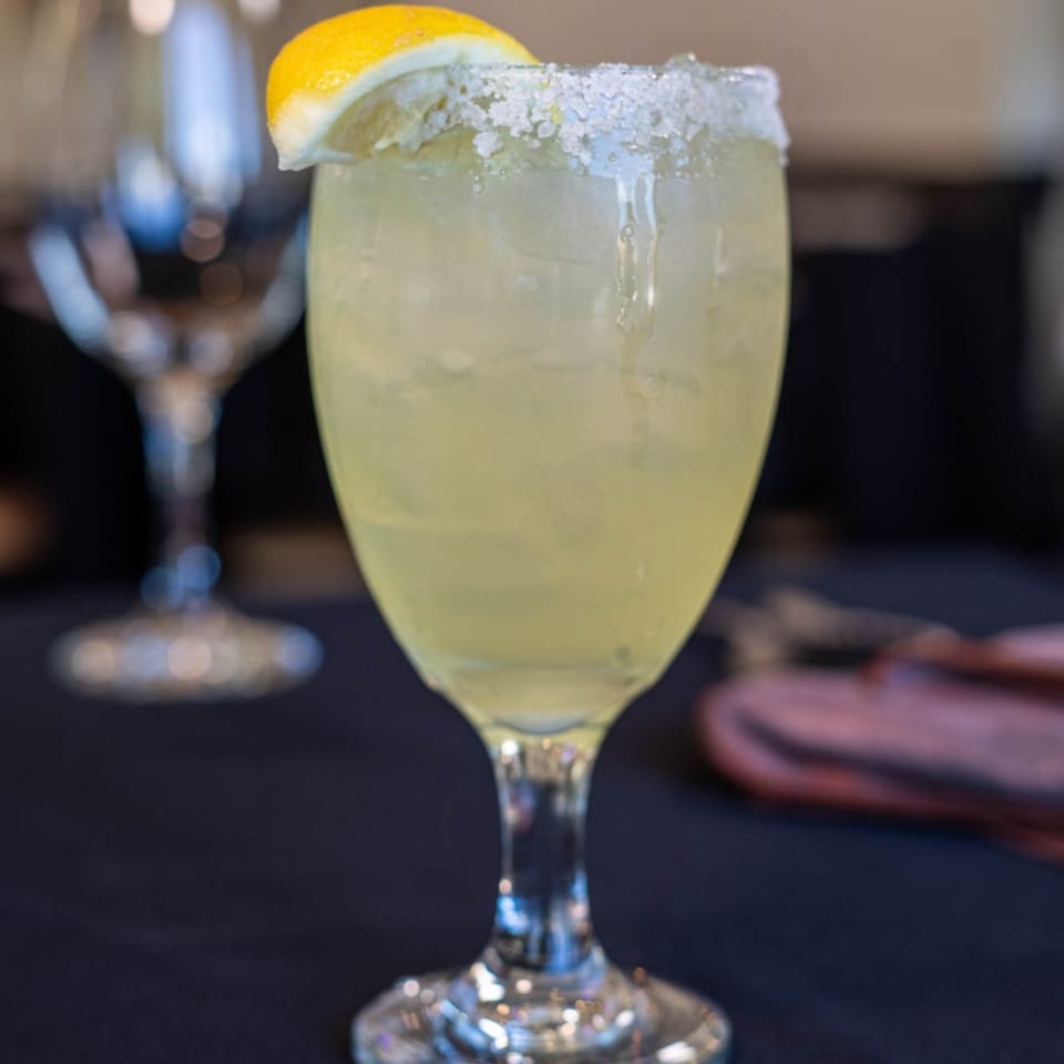 A Bendita Cocina margarita with a salted rim and lemon wedge, on a dark table.