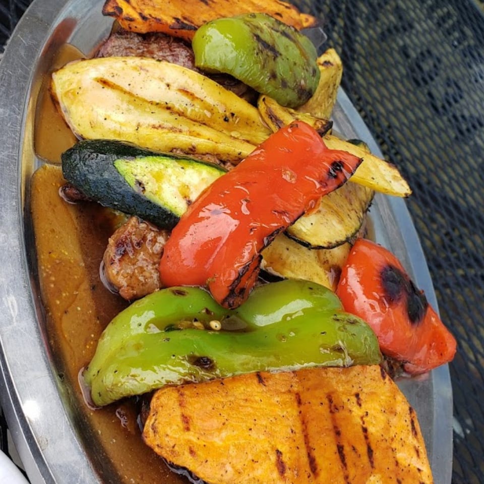 Grilled vegetables and meat, including red and green peppers, zucchini, and sweet potatoes, on a silver platter.