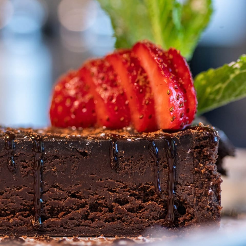 Rich chocolate brownie drizzled with sauce, topped with sliced strawberries and mint.