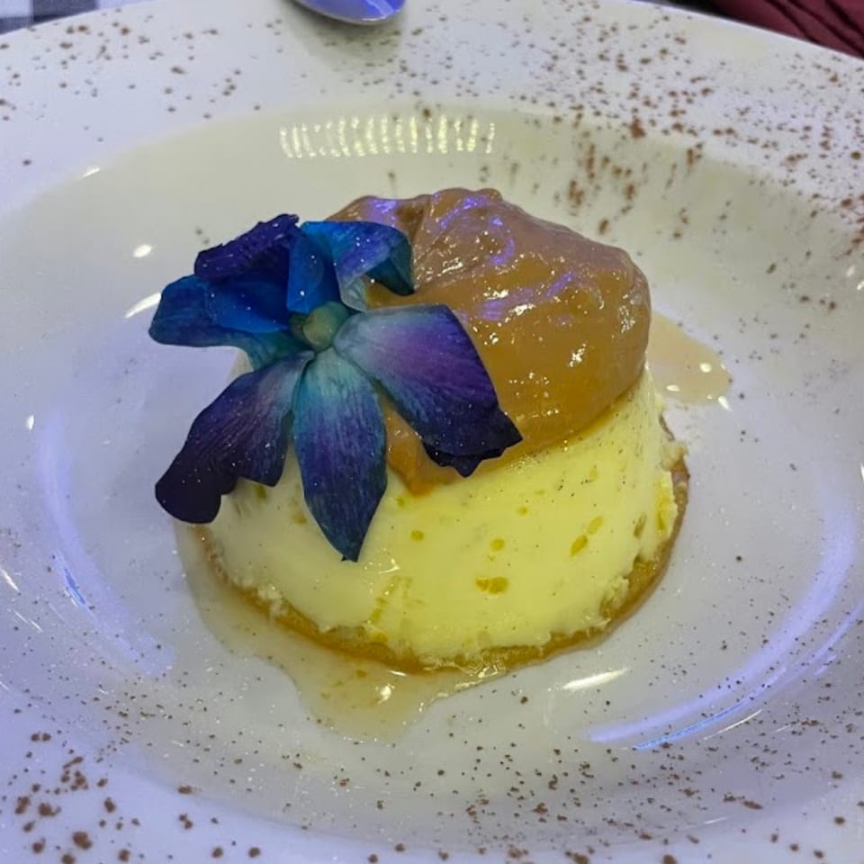 Flan with dulce de leche and a blue orchid on a white plate at Bendita Cocina.